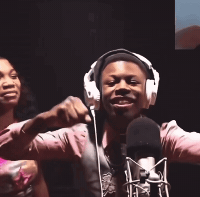 A Man Wearing Headphones Stands In Front Of A Microphone With His Hands In The Air GIF