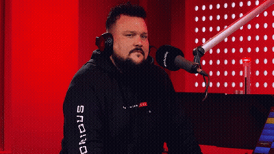 A Man Wearing Headphones Stands In Front Of A Microphone With The Word Snc On His Sleeve GIF