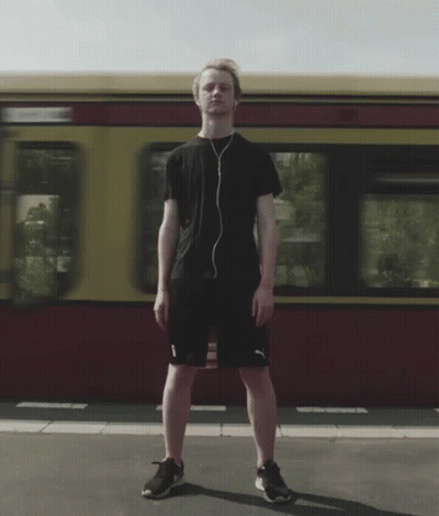 A Man Wearing Headphones Stands In Front Of A Red And Yellow Train GIF