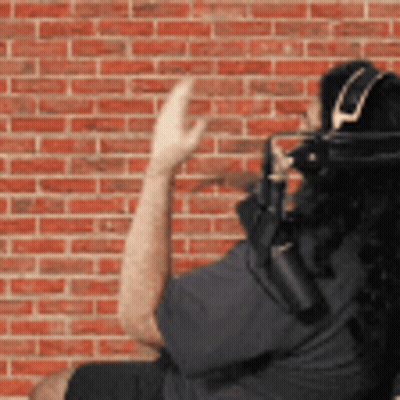 A Man Wearing Headphones Stands In Front Of A Red Brick Wall GIF