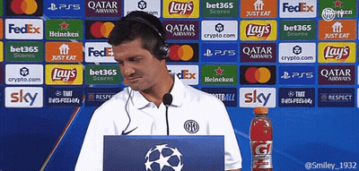 A Man Wearing Headphones Stands In Front Of A Wall Of Advertisements Including Lays And Sky GIF