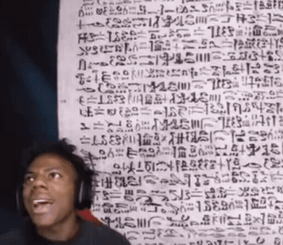 A Man Wearing Headphones Stands In Front Of A Wall With Ancient Writing GIF