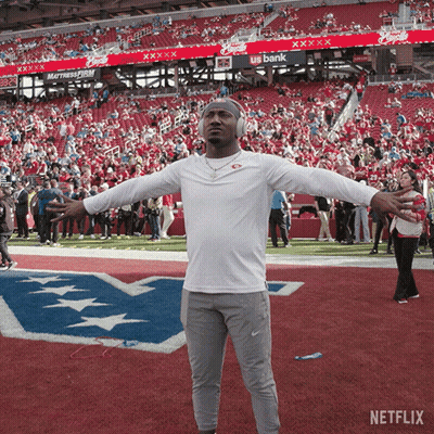 A Man Wearing Headphones Stands On A Football Field With His Arms Outstretched In Front Of A Us Bank Banner GIF