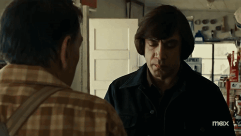 A Man Wearing Headphones Talks To Another Man In A Store With Max Written On The Bottom Right GIF