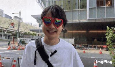A Man Wearing Heart Shaped Sunglasses Is Smiling In Front Of A Large Building GIF