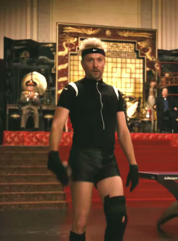 A Man Wearing Knee Pads And A Nike Headband Stands In Front Of A Ping Pong Table GIF