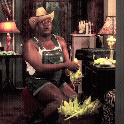 A Man Wearing Overalls And A Cowboy Hat Holds Corn On The Cob In His Hands GIF