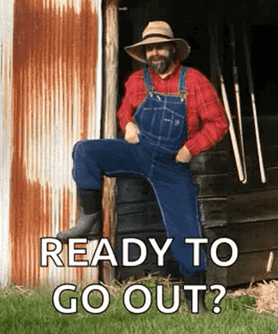 A Man Wearing Overalls And A Hat Is Sitting On A Fence . GIF