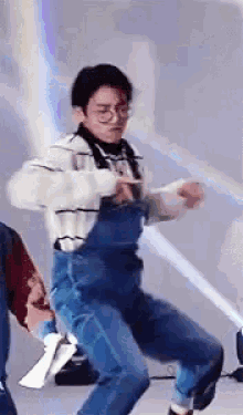 A Man Wearing Overalls And Glasses Is Dancing In A Room . GIF