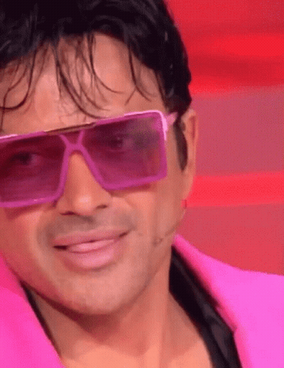 A Man Wearing Pink Sunglasses And A Pink Jacket Smiles GIF