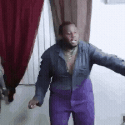A Man Wearing Purple Pants And A Blue Jacket Is Dancing In A Room . GIF