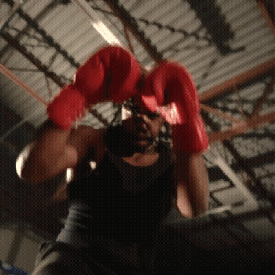 A Man Wearing Red Boxing Gloves Is Hanging From A Ceiling GIF