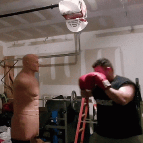 A Man Wearing Red Boxing Gloves Is Standing In Front Of A Mannequin GIF