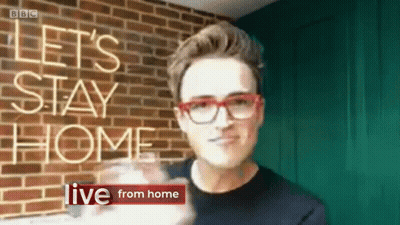 A Man Wearing Red Glasses Stands In Front Of A Brick Wall With The Words Let 'S Stay Home Live From Home GIF