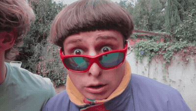 A Man Wearing Red Sunglasses And A Blue Jacket Makes A Surprised Face GIF