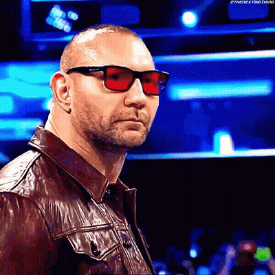 A Man Wearing Red Sunglasses And A Leather Jacket Is Standing In Front Of A Crowd . GIF