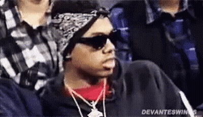 A Man Wearing Sunglasses , A Bandana And A Necklace Is Sitting In A Crowd Of People . GIF