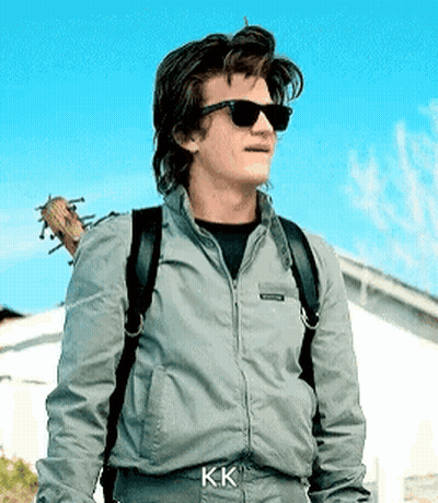 A Man Wearing Sunglasses And A Backpack Is Standing In Front Of A House . GIF