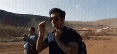 A Man Wearing Sunglasses And A Backpack Is Walking Through A Desert . GIF