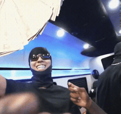 A Man Wearing Sunglasses And A Balaclava Is Smiling In Front Of A Pile Of Money GIF