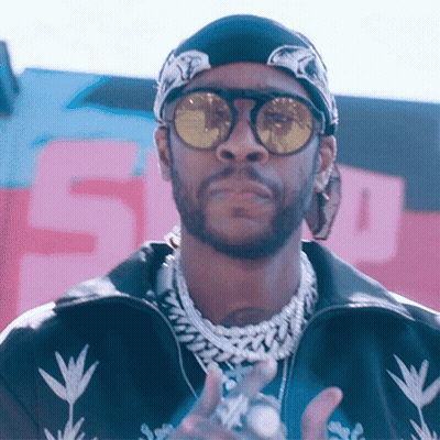 A Man Wearing Sunglasses And A Bandana Stands In Front Of A Sign That Says 5 GIF