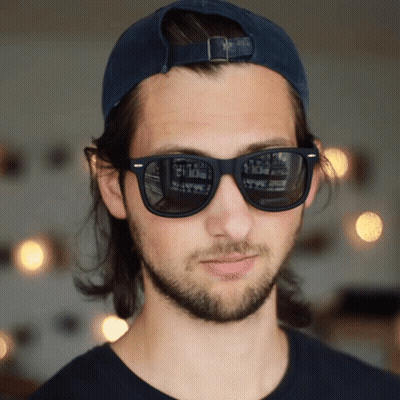 A Man Wearing Sunglasses And A Baseball Cap Has A Reflection Of A Building In His Sunglasses GIF