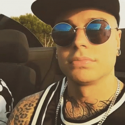 A Man Wearing Sunglasses And A Baseball Cap Is Sitting In A Car GIF
