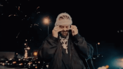 A Man Wearing Sunglasses And A Beanie Is Standing In Front Of Fireworks . GIF