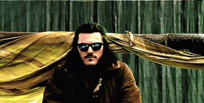 A Man Wearing Sunglasses And A Beard Is Standing In Front Of A Green Curtain GIF