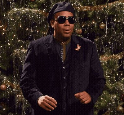 A Man Wearing Sunglasses And A Black Hat Is Dancing In Front Of A Christmas Tree GIF