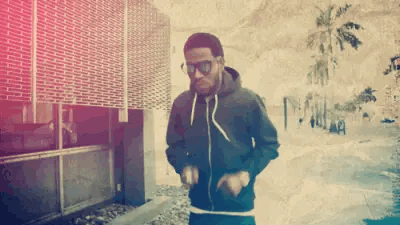 A Man Wearing Sunglasses And A Black Hoodie Is Dancing On The Sidewalk . GIF