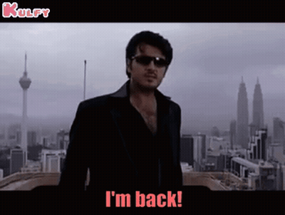 A Man Wearing Sunglasses And A Black Jacket Is Standing In Front Of A City And Says I 'M Back . GIF