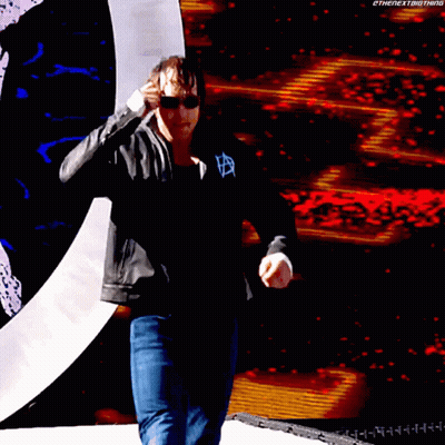 A Man Wearing Sunglasses And A Black Jacket Stands In Front Of A Large Screen That Says Thenextbigthing GIF