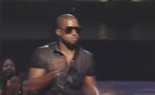 A Man Wearing Sunglasses And A Black Shirt Is Holding A Microphone In His Right Hand GIF