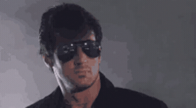 A Man Wearing Sunglasses And A Black Shirt Is Looking At The Camera . GIF
