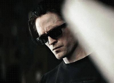 A Man Wearing Sunglasses And A Black Shirt Is Looking Down At Something . GIF