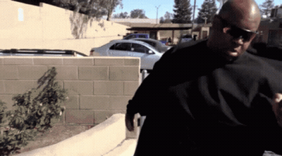 A Man Wearing Sunglasses And A Black Shirt Is Standing In A Parking Lot GIF