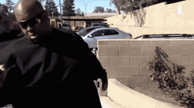 A Man Wearing Sunglasses And A Black Shirt Is Standing Next To A Brick Wall GIF