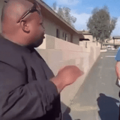 A Man Wearing Sunglasses And A Black Shirt Is Standing Next To A Brick Wall . GIF