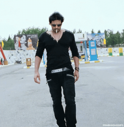 A Man Wearing Sunglasses And A Black Shirt Is Walking Down The Street GIF