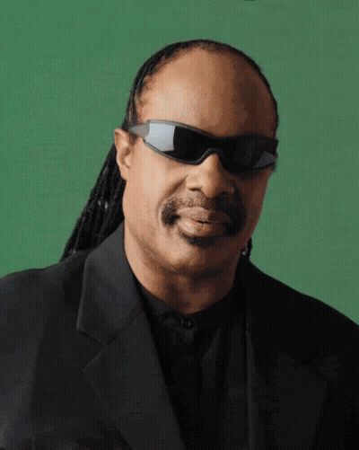 A Man Wearing Sunglasses And A Black Suit Is Smiling GIF