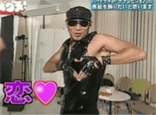 A Man Wearing Sunglasses And A Black Vest Is Standing In Front Of A Pink Heart With Chinese Writing On It GIF