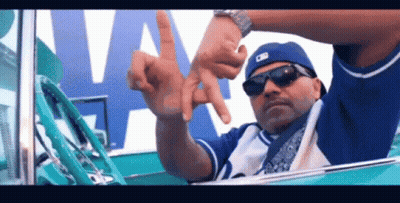 A Man Wearing Sunglasses And A Blue Hat Is Sitting In A Car And Making A Peace Sign With His Hands . GIF