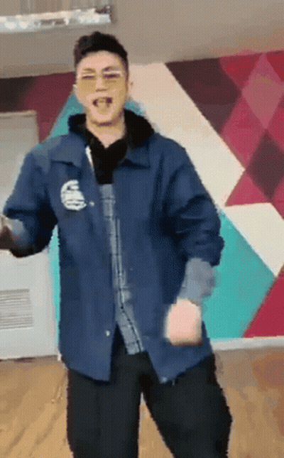 A Man Wearing Sunglasses And A Blue Jacket Is Dancing In Front Of A Wall . GIF