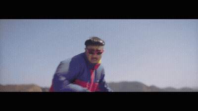 A Man Wearing Sunglasses And A Blue Jacket Is Standing In The Desert GIF