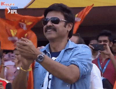 A Man Wearing Sunglasses And A Blue Shirt Is Clapping His Hands In Front Of A Crowd . GIF