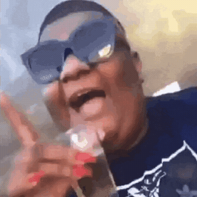 A Man Wearing Sunglasses And A Blue Shirt Is Holding A Glass In His Hand . GIF