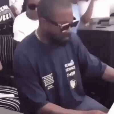 A Man Wearing Sunglasses And A Blue Shirt Is Sitting At A Table In A Crowd . GIF