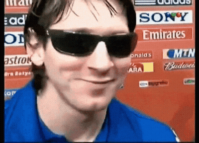 A Man Wearing Sunglasses And A Blue Shirt Is Smiling In Front Of A Sign That Says Sony Emirates GIF