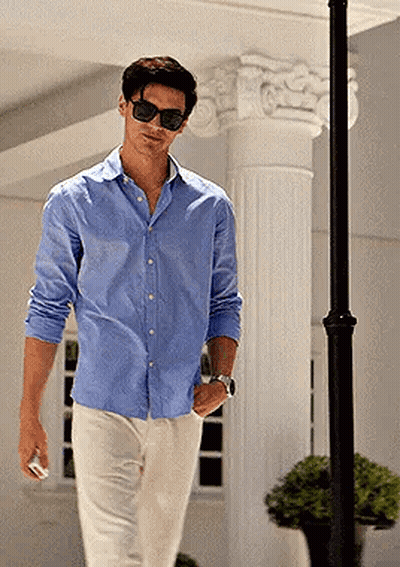 A Man Wearing Sunglasses And A Blue Shirt Is Walking Down A Street GIF